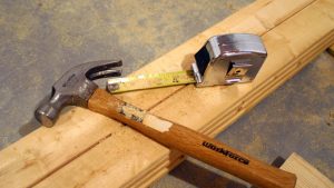 A hammer and measuring tape on a wood bench